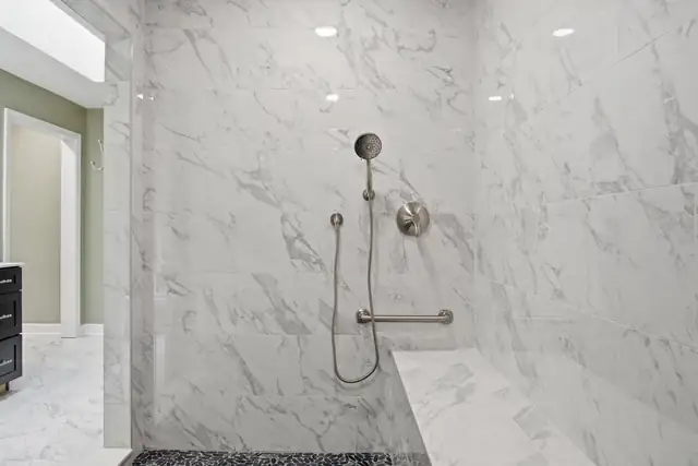 Large walk-in shower with marble-look tile, built-in bench, grab bar and handheld shower in a Blacksburg primary bath