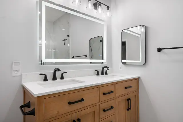 Christiansburg bathroom with a natural wood double vanity, black faucets and a lighted mirror