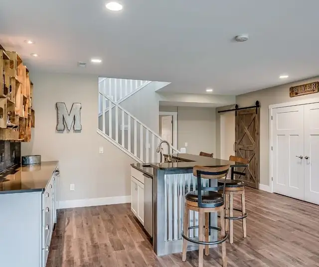 Finished basement bar with corrugated metal bar front, wood stools, barn door and stair to the main floor