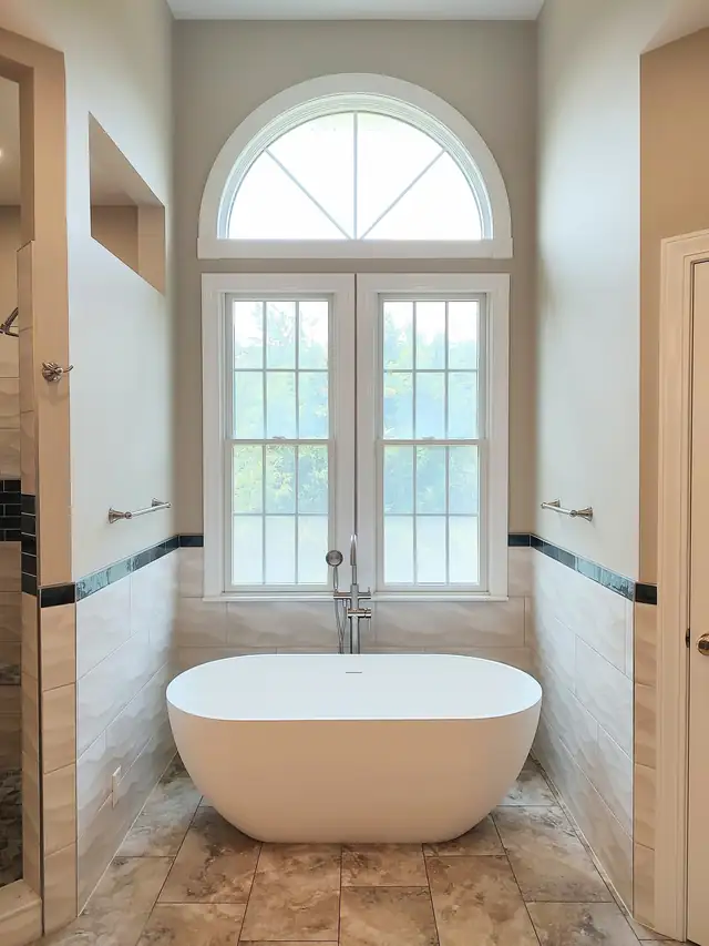 Riner primary bath with a freestanding tub under an arched window and blue accent tile band