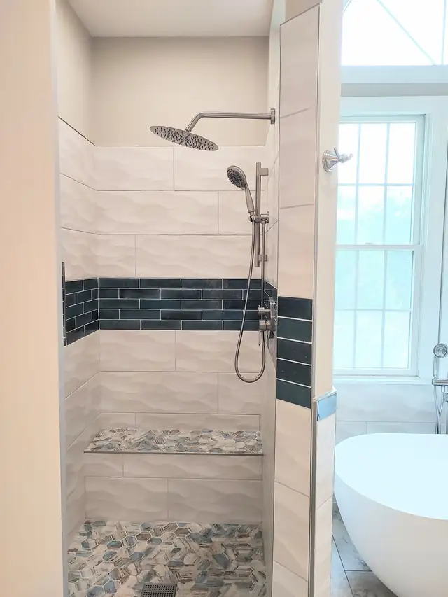 Riner walk-in shower with white wave tile, navy tile band, rain head and pebble floor